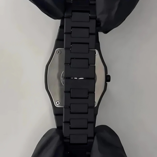 Close-up of a black watch with a metallic back plate on a light gray background