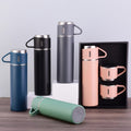 Collection of stainless steel thermos bottles and mugs on a wooden surface with a light gray background.