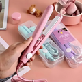 Pink hair straightener held by a hand on a pink surface with beauty products in the background.