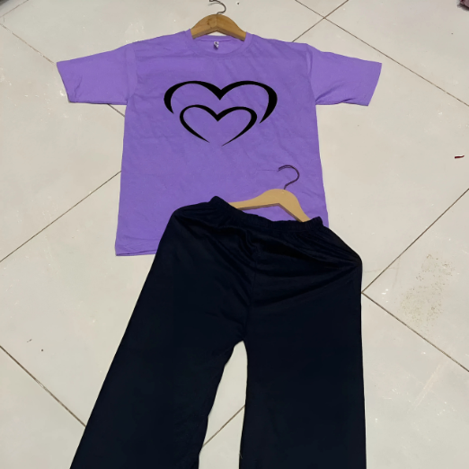 Purple t-shirt with heart design and black pants on a hanger against a white wall.