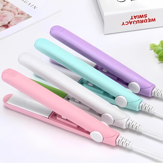 Set of colorful hair straighteners on a white surface with a magazine and plant in the background.