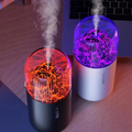 Two colorful humidifiers emitting mist on a wooden surface with a laptop in the background.