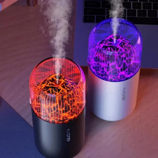Two colorful humidifiers emitting mist on a wooden surface with a laptop in the background.