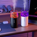Two humidifiers emitting mist on a desk with a laptop and mouse in the background.