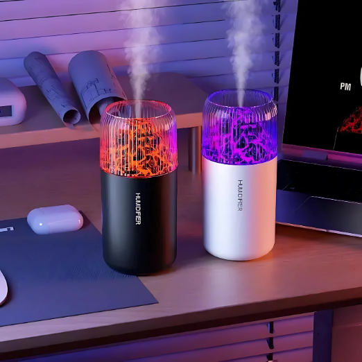 Two humidifiers emitting mist on a desk with a laptop and mouse in the background.