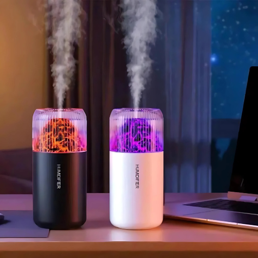 Two humidifiers emitting mist on a desk with a laptop in the background.