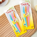 Two packages of Tinkle toothbrushes on a wooden surface