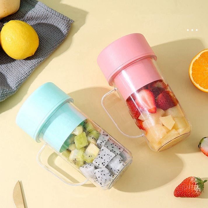 Green tumbler with fruit, glass of juice, and bowl of berries on a wooden table.
