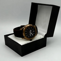 Watch with black strap and bronze case in a black box on a gray background