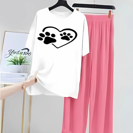 White shirt with black paw print design and pink pants on a hanger against a white wall.