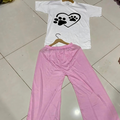 White shirt with black paw print design and pink pants on a tiled floor.