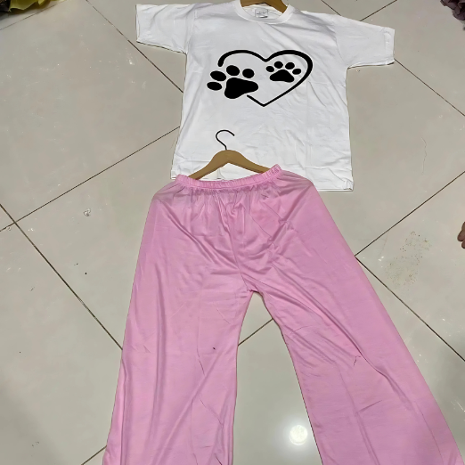 White shirt with black paw print design and pink pants on a tiled floor.