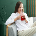 Woman sitting on a couch drinking from a pink tumbler with a green background