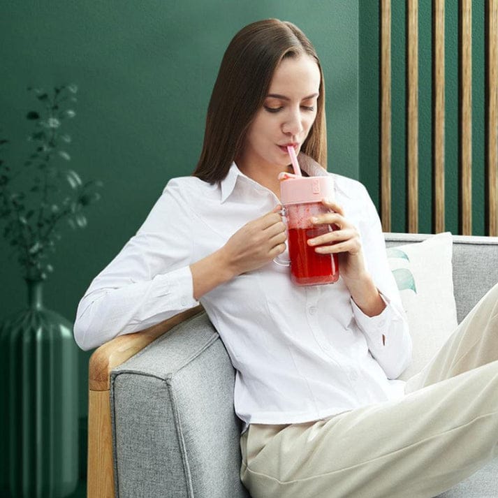 Woman sitting on a couch drinking from a pink tumbler with a green background