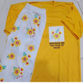 Yellow t-shirt with floral design and text, next to a white towel with floral patterns on a white background.